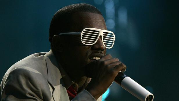 Kanye West mit einer Lamellenbrille singt in ein Mikrofon.