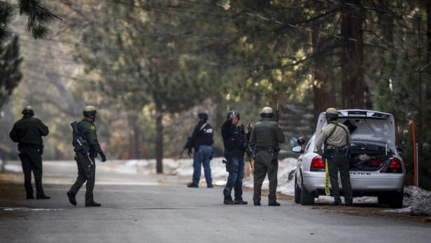 epa03573023 Officers walk door to door searching for murder suspect Christopher Jordan Dorner in Big Bear Lake, California, USA 07 February 2013. A former policeman with a grudge against his superiors has gone on a rampage through Los Angeles in which he is suspected of killing three people and shooting three policemen. A huge manhunt was underway for Christopher Jordan Dorner, 33, who released a chilling manifesto earlier in the week threatening to target police in retribution for being fired. EPA/BRET HARTMAN