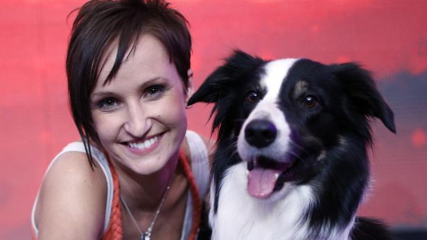 Eine lächelnde Frau posiert mit ihrem Border Collie vor einem roten Hintergrund.