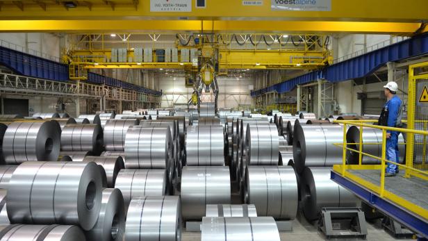 Ein Arbeiter in einer Fabrikhalle mit vielen Stahlrollen und einem Kran von Voestalpine.