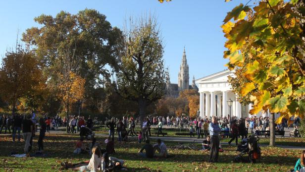 Der Wiener Rathauspark im Herbst mit vielen Menschen und dem Rathaus im Hintergrund.