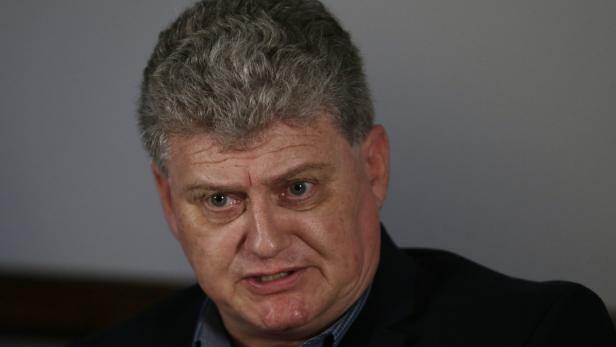 Porträt eines Mannes mit grauem Haar und einem dunklen Anzug.