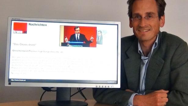 Ein Mann sitzt neben einem Monitor, der Nachrichten von krone.at anzeigt.