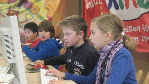 Vier Kinder sitzen vor einem Computer und schauen auf den Bildschirm.