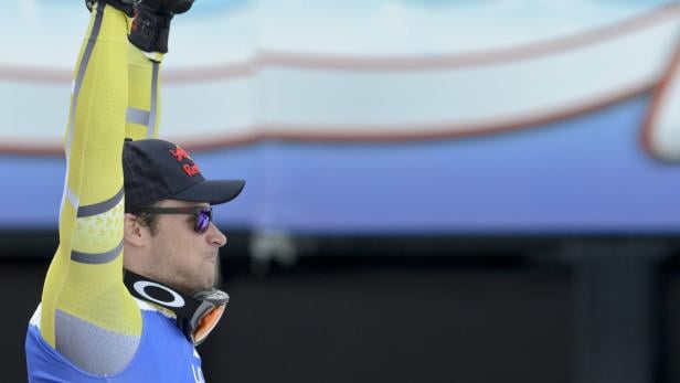 Ein Skirennläufer mit Sonnenbrille und Kappe hebt die Arme.