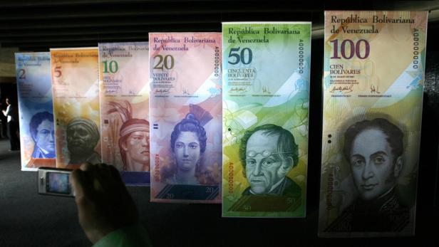 Eine Person fotografiert eine Ausstellung venezolanischer Banknoten unterschiedlicher Werte.