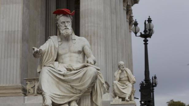 Eine Statue vor dem Parlament in Wien mit einem roten Hut auf dem Kopf.