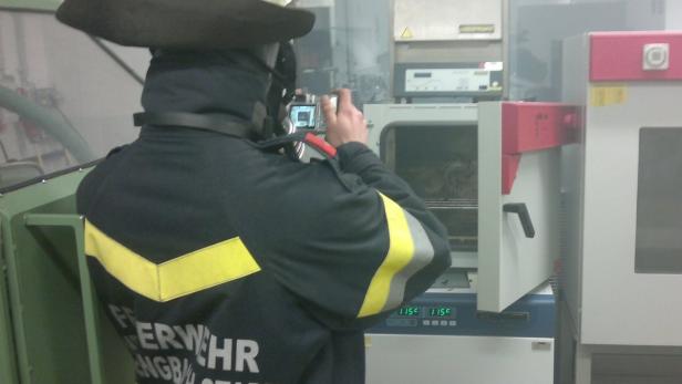 Ein Feuerwehrmann fotografiert mit einer Digitalkamera einen Ofen.