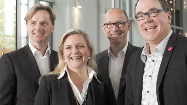 Eine Gruppe von vier lächelnden Personen in Anzügen posiert für ein Foto.