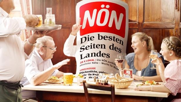 Gäste sitzen in einem Wirtshaus an einem Tisch, an dem eine Person im NÖN-Kostüm steht.
