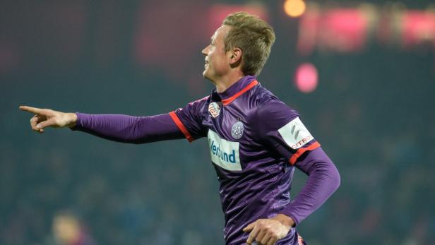 Ein Fußballspieler in lila Trikot zeigt mit dem Finger nach links.
