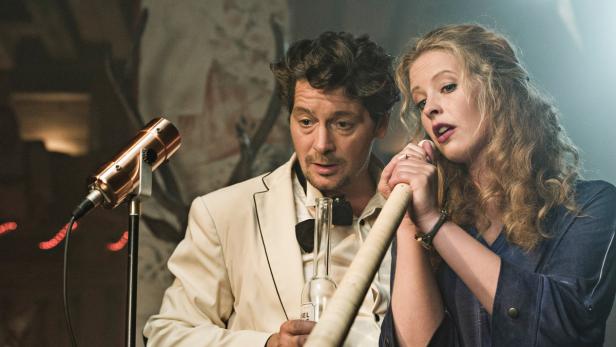 Ein Mann im Anzug und eine Frau singen zusammen an einem alten Mikrofon.