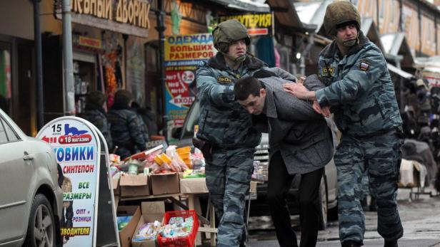 Zwei Polizisten führen einen Mann in Zivil auf einer belebten Straße ab.