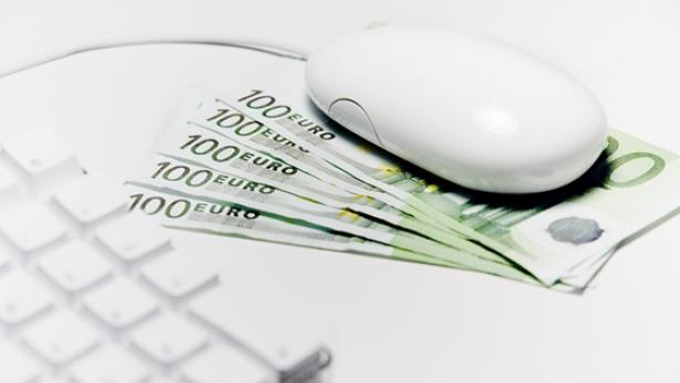 Eine Computermaus liegt auf einem Stapel von 100-Euro-Scheinen neben einer Tastatur.