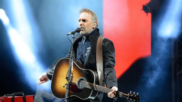 Kevin Costner tritt mit seiner Gitarre auf einer Bühne auf.