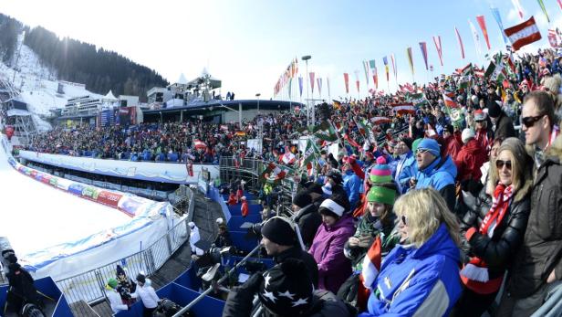 Eine große Menschenmenge jubelt bei einem Ski-Event mit vielen Flaggen im Schnee.