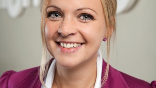 Eine lächelnde Frau mit blonden Haaren und einem pinkfarbenen Blazer.