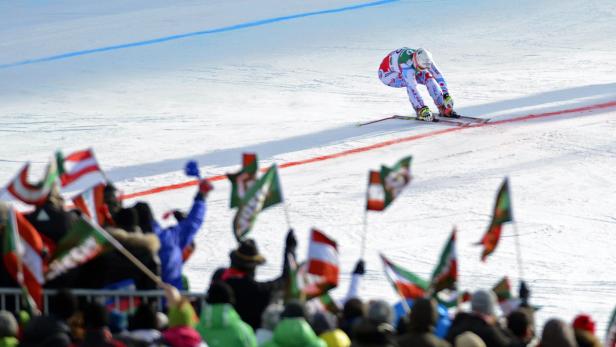 Ein Skirennläufer fährt an einer Zuschauermenge mit Flaggen vorbei.