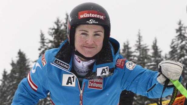 Eine Skifahrerin mit Helm und Sponsorenlogos vor verschneiten Bäumen.