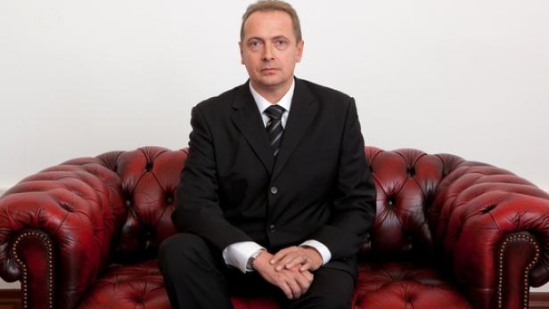 Ein Mann im Anzug sitzt auf einem roten Ledersofa.