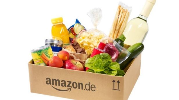 Ein Amazon.de-Karton gefüllt mit Lebensmitteln wie Obst, Gemüse, Nudeln und einer Flasche Wein.