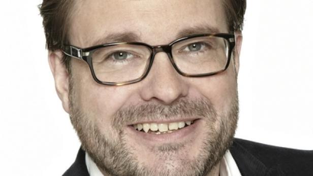 Ein lächelnder Mann mit Brille und Bart vor einem weißen Hintergrund.