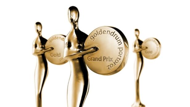 Drei goldene „Golden Drum Grand Prix“-Trophäen vor einem weißen Hintergrund.