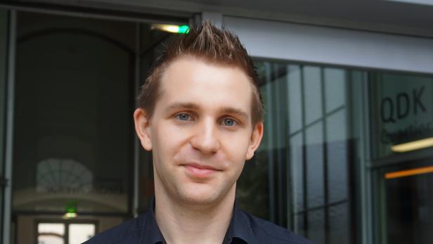 Ein junger Mann mit blonden Haaren und blauem Hemd blickt in die Kamera.