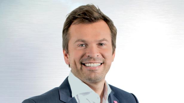 Ein lächelnder Mann im Anzug vor einem hellen Hintergrund.