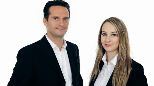 Ein Mann und eine Frau in Anzügen posieren vor einem weißen Hintergrund.