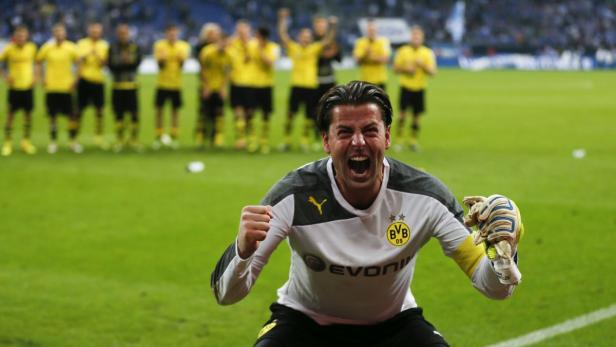 Ein jubelnder Torwart von Borussia Dortmund auf dem Rasen, im Hintergrund die Mannschaft.