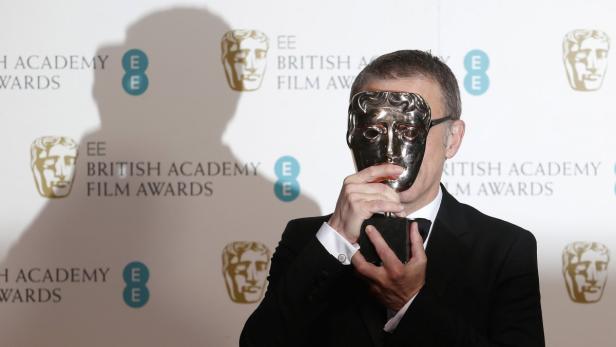 Ein Mann hält eine BAFTA-Trophäe vor sein Gesicht.