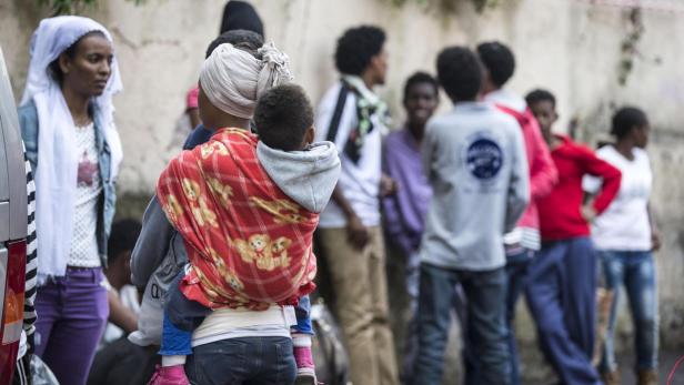 Eine Frau trägt ein Kind in einer Trage vor einer Gruppe von Menschen.