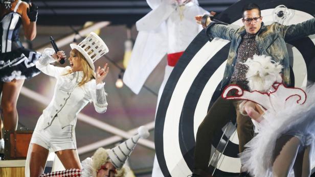 Taylor Swift tritt in einem weißen Anzug und Zylinder auf einer Bühne auf.