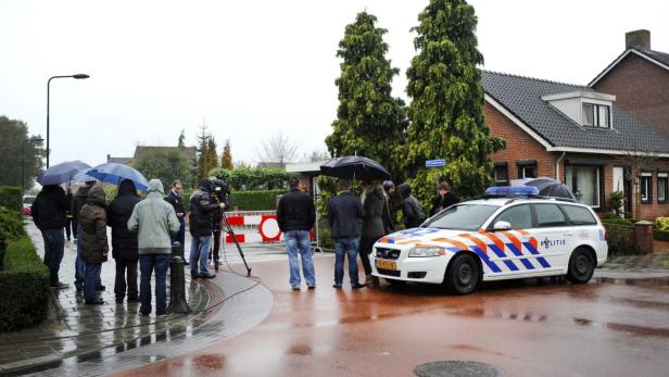 Eine Gruppe von Menschen steht bei Regen vor einem Haus, in der Nähe ein Polizeiauto.