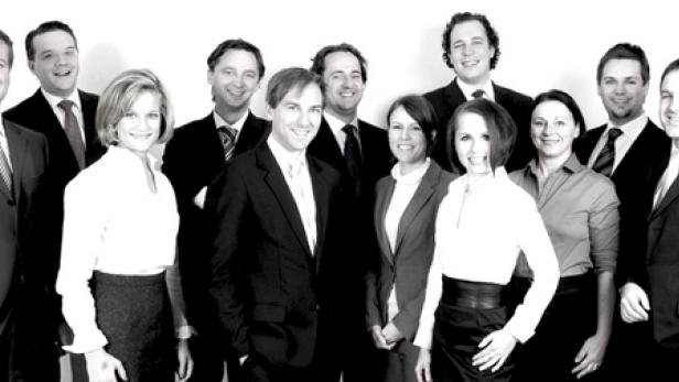 Eine Gruppe von elf Personen in formeller Kleidung posiert für ein Gruppenfoto.