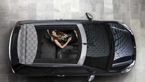 Eine Frau liegt auf dem Rücksitz eines schwarzen Autos mit offenem Panoramadach.