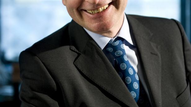 Ein lächelnder Mann mit Brille und Anzug vor einem Fenster.