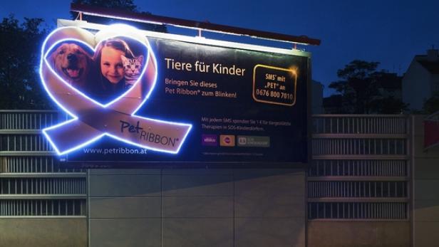 Eine beleuchtete Werbetafel wirbt für „Pet Ribbon“ und „Tiere für Kinder“.