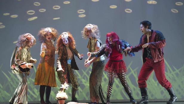 Eine Gruppe von maskierten Darstellern in Kostümen auf einer Bühne.