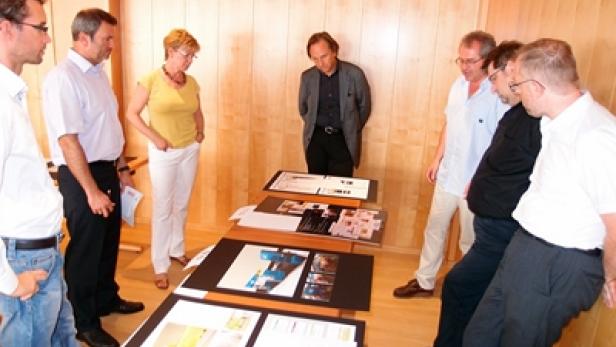 Eine Gruppe von Personen betrachtet Pläne und Entwürfe auf einem Tisch.
