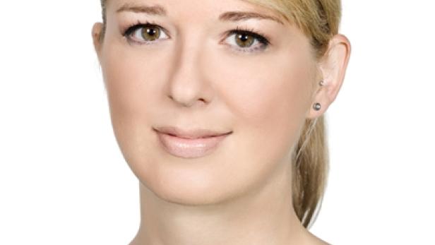 Porträt einer blonden Frau mit braunen Augen vor einem weißen Hintergrund.