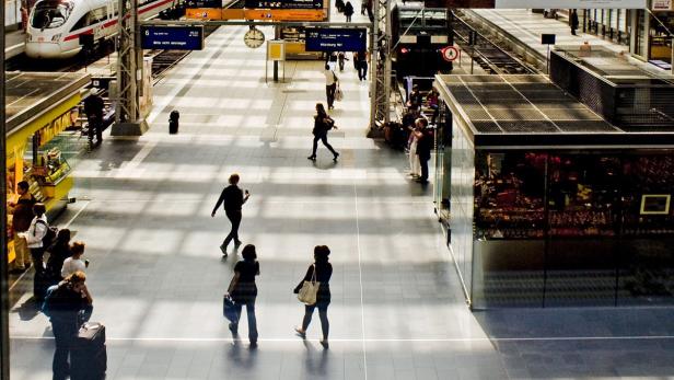 Menschen gehen in einer hellen Bahnhofshalle umher.