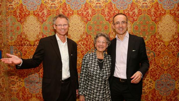 Drei Personen posieren vor einem farbenprächtigen Wandteppich.