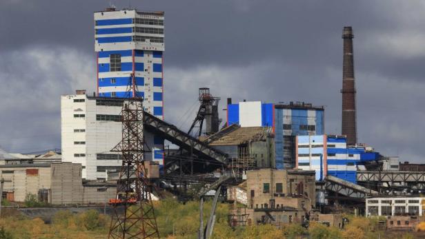 Eine Industrieanlage mit einem hohen Schornstein und einem blau-weiß gestreiften Turm unter einem bewölkten Himmel.