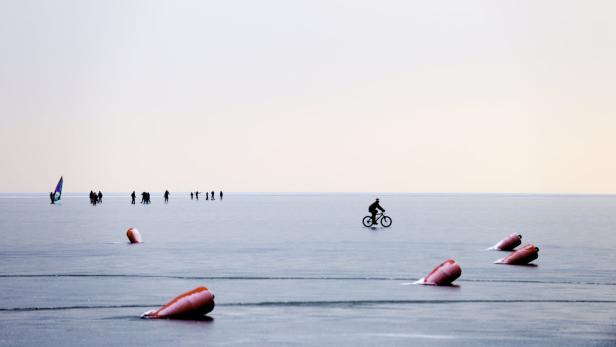 AUSTRIA / BURGENLAND / LAKE NEUSIEDL / NEUSIEDL ON THE LAKE / MOLE WEST icebound buoys and bicyclist near the pub &quot;Mole West&quot; and ice skaters © Manfred HORVATH