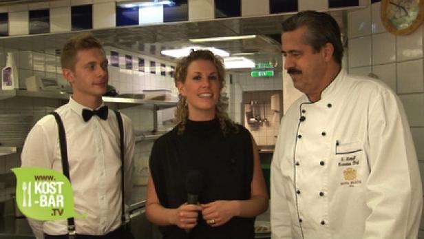 Eine Frau interviewt einen Koch und einen Kellner in einer Restaurantküche.