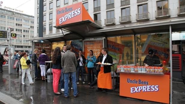 Ein „Uncle Ben's Express“-Stand auf einer belebten Straße mit wartenden Menschen.