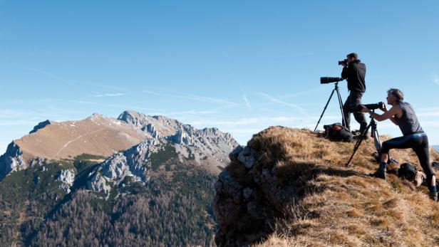 Zwei Fotografen fotografieren mit Stativen eine Berglandschaft.