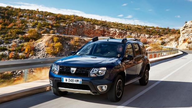 Ein blauer Dacia Duster fährt auf einer kurvenreichen Straße entlang einer Hügellandschaft.